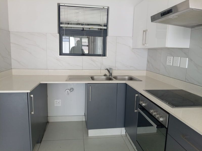 Modern kitchen featuring sleek grey and white cabinetry, stone countertops, integrated electric hob, oven, extractor fan, and tiled backsplash.