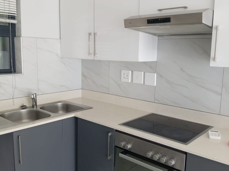 Modern kitchen featuring sleek two-tone cabinetry, stone countertops, marble-look tile backsplash, and integrated stainless steel appliances including an oven, hob, and extractor fan.
