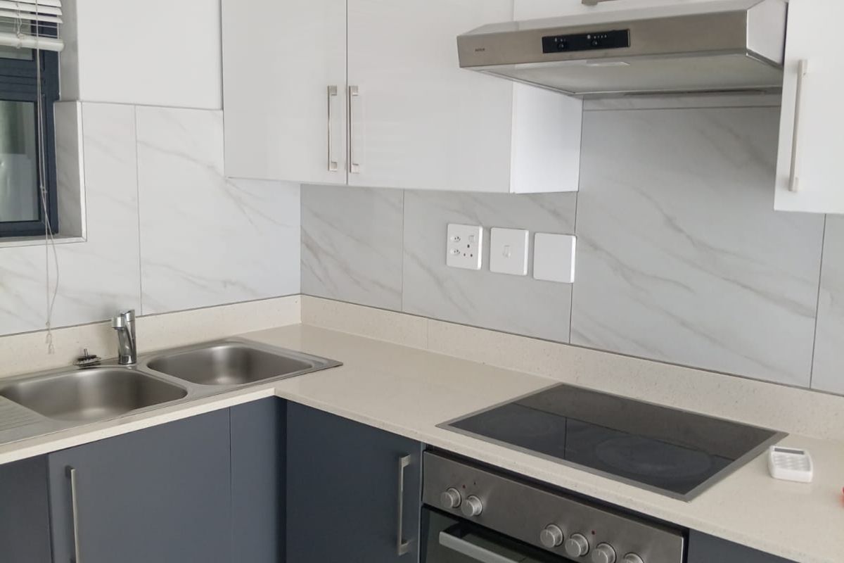 Modern kitchen featuring sleek two-tone cabinetry, stone countertops, marble-look tile backsplash, and integrated stainless steel appliances including an oven, hob, and extractor fan.