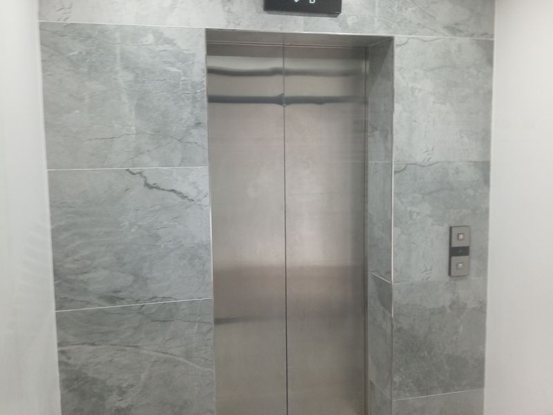 A modern apartment building hallway featuring a stainless steel elevator with elegant grey stone wall cladding and neutral floor tiles.