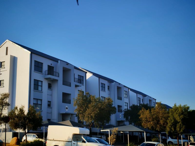 Exterior view of a multi-story apartment complex featuring white facades, private balconies, and covered parking structures.