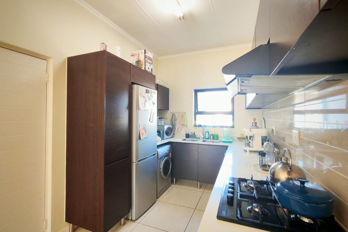 A functional kitchen featuring dark wood cabinetry, a gas hob with extractor fan, tiled flooring, and a double sink with a tiled backsplash.