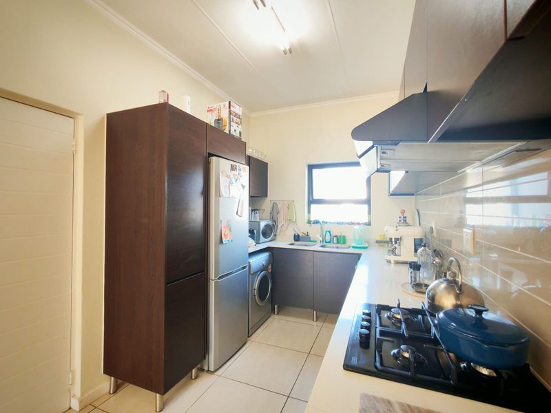 A functional kitchen featuring dark wood cabinetry, a gas hob with extractor fan, tiled flooring, and a double sink with a tiled backsplash.