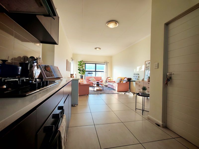 An open-plan living area featuring a modern kitchen with built-in cabinetry and gas hob, flowing into a bright, tiled lounge space.