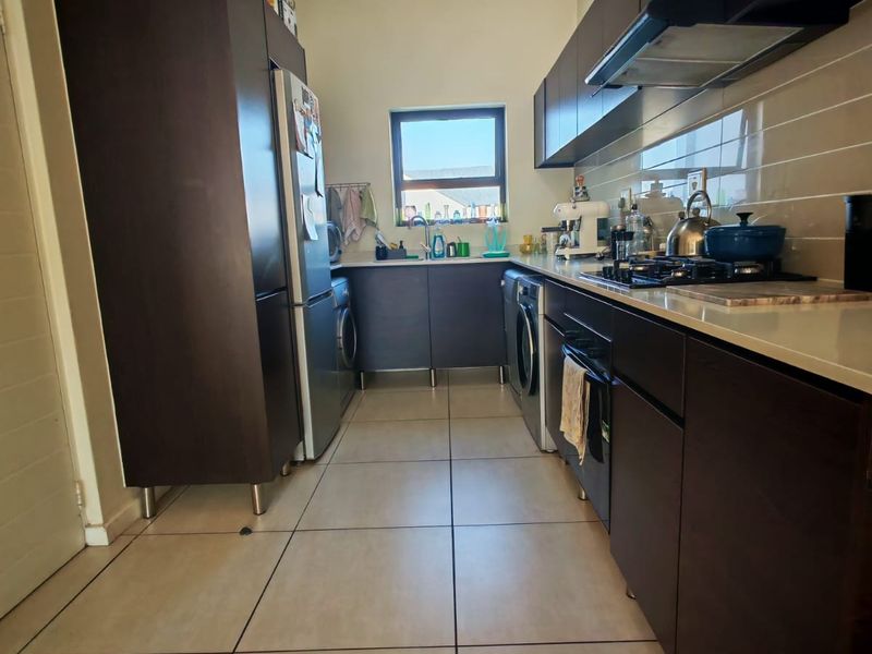 A functional kitchen featuring dark wood cabinetry, stone countertops, a gas hob with extractor fan, and tiled flooring.