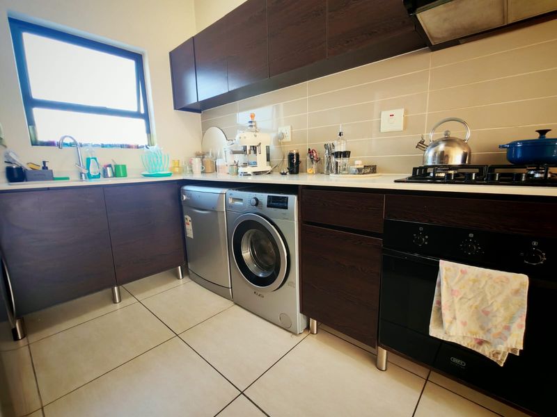 Modern kitchen featuring dark wood cabinetry, built-in oven, gas hob, extractor fan, tiled backsplash, and tiled flooring.