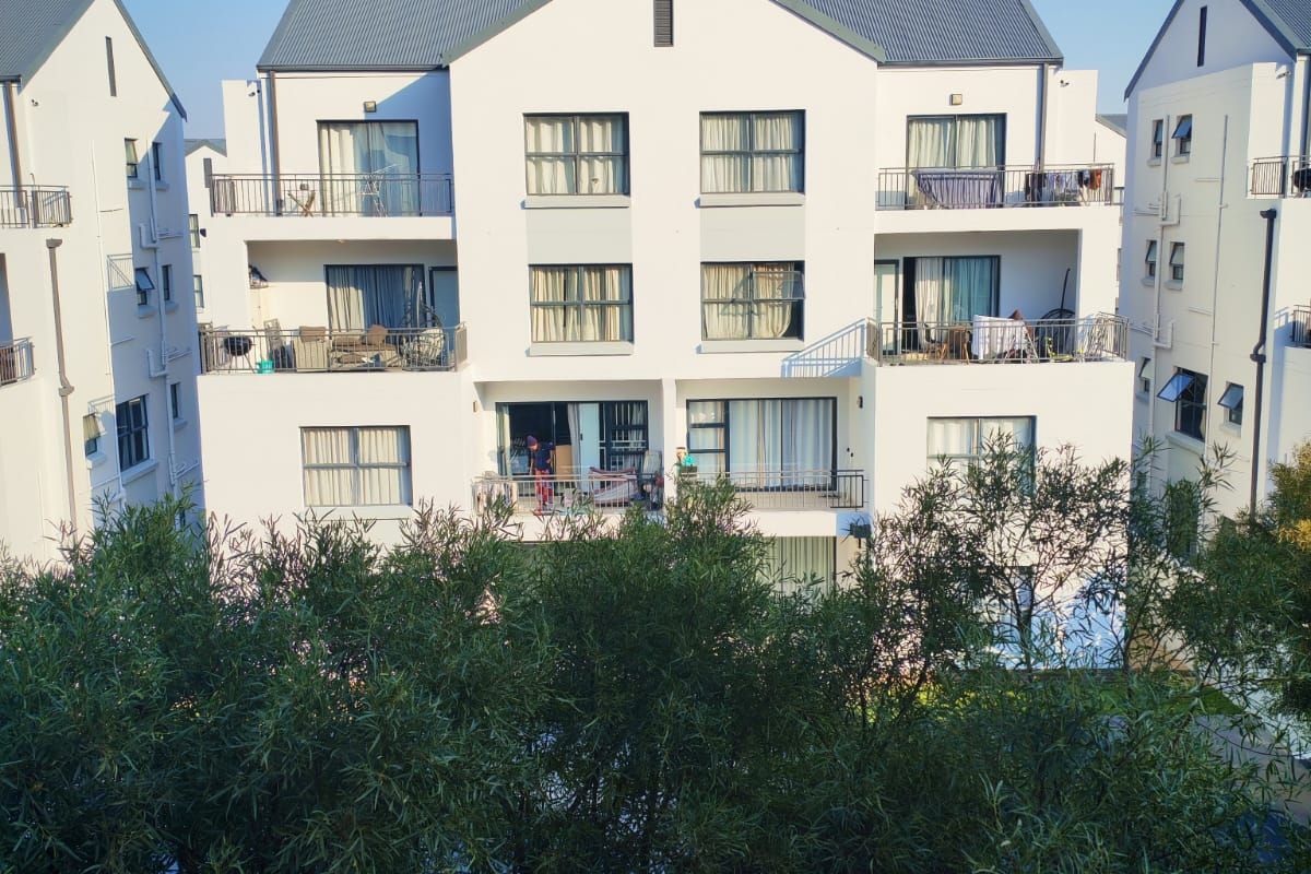 A view of the rear elevation of a multi-story apartment complex featuring balconies, sliding glass doors, and a pitched metal roof.
