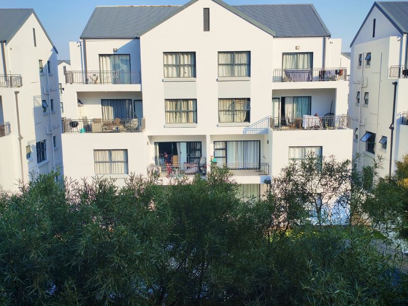 A view of the rear elevation of a multi-story apartment complex featuring balconies, sliding glass doors, and a pitched metal roof.