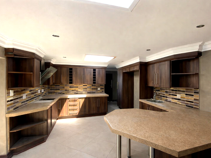 Spacious kitchen featuring dark wood cabinetry, stone countertops, mosaic tile backsplash, a breakfast bar, and a large skylight providing ample natural light.