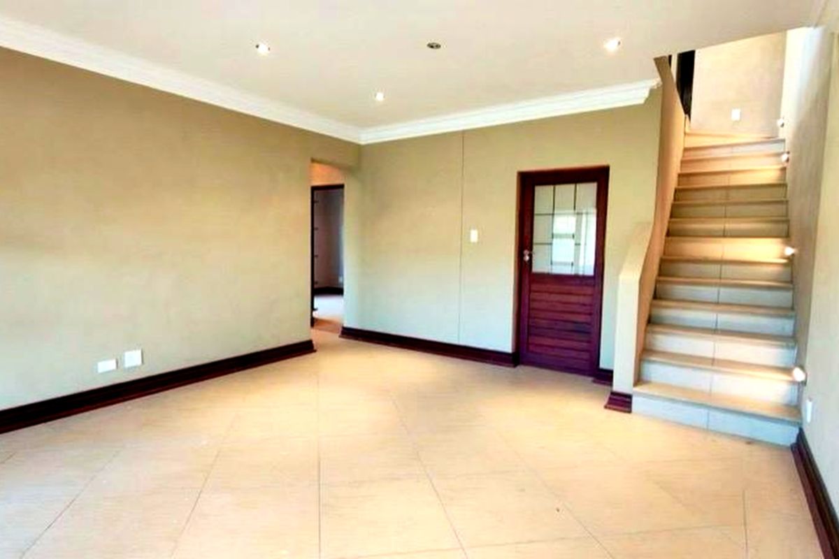 An empty, well-lit living area featuring tiled flooring, recessed downlights, and a staircase leading to the upper level.