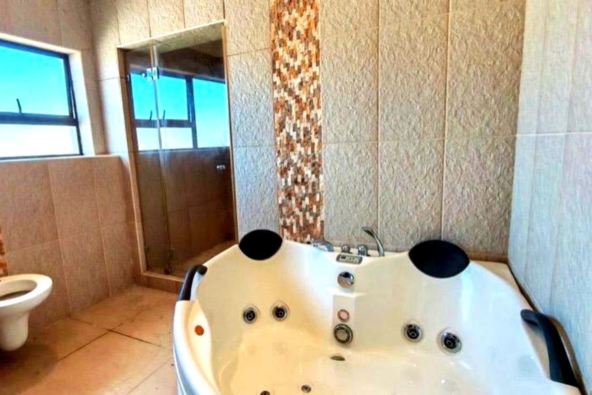 A spacious bathroom featuring a corner spa bath, a separate glass-enclosed shower, and a wall-mounted toilet with decorative mosaic tile accents.