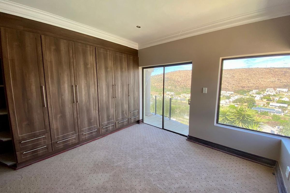 Spacious bedroom featuring extensive built-in wooden cupboards, carpeted flooring, and a sliding glass door opening to a balcony with scenic views.
