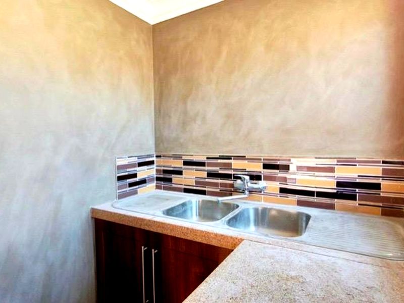 A functional scullery area featuring a double bowl stainless steel sink, modern mixer tap, tiled splashback, and built-in cabinetry with stone-look countertops.
