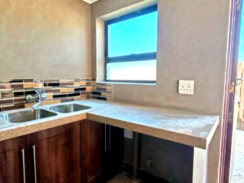 A functional scullery area featuring dark wood cabinetry, a double bowl stainless steel sink, and a stone-look countertop with a tiled splashback.