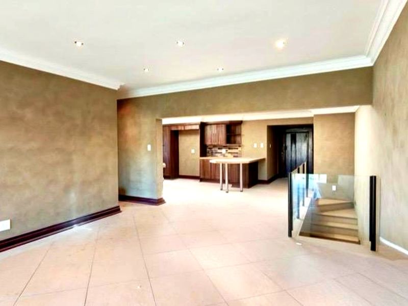 Spacious open-plan living area featuring tiled floors, recessed lighting, crown molding, and a glass-railed staircase leading to the lower level.