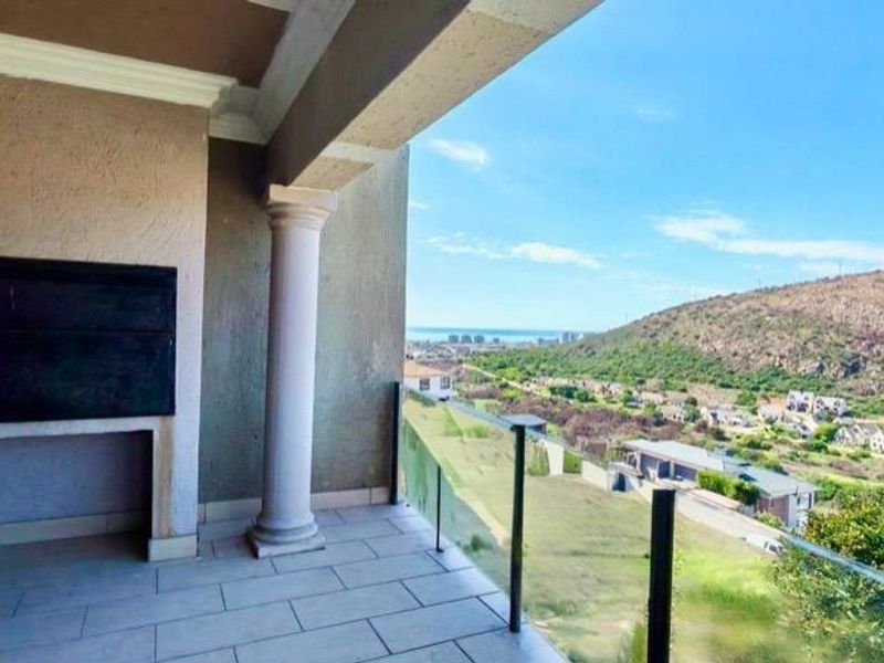 Covered balcony featuring a built-in braai, glass balustrade, and expansive elevated views of the surrounding landscape and coastline.