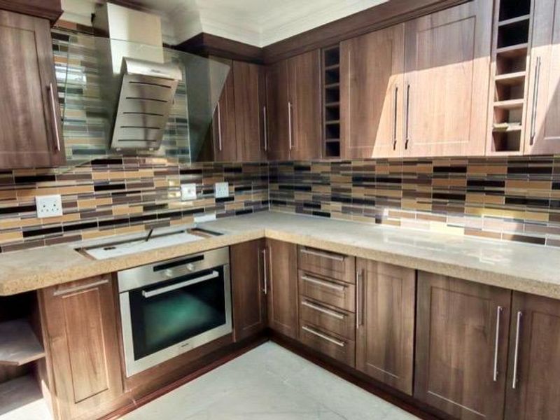 Modern kitchen featuring dark wood cabinetry, stone countertops, a built-in oven, stainless steel extractor fan, and a decorative mosaic tile backsplash.
