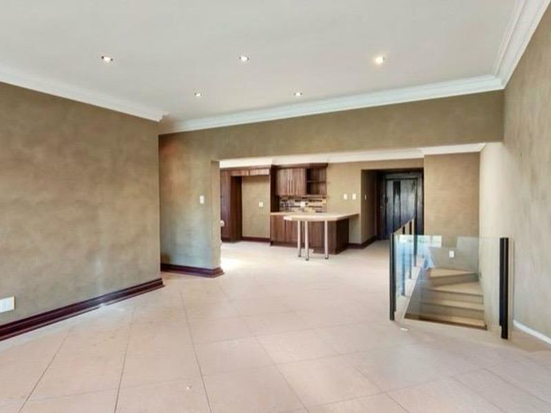 Spacious open-plan living area featuring tiled floors, recessed lighting, crown molding, and a modern glass balustrade overlooking the staircase, with an integrated kitchen area.