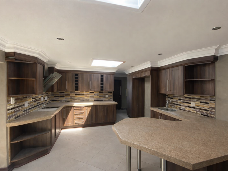 Spacious kitchen featuring dark wood cabinetry, stone-look countertops, mosaic tile backsplash, a breakfast bar, and a skylight for natural illumination.