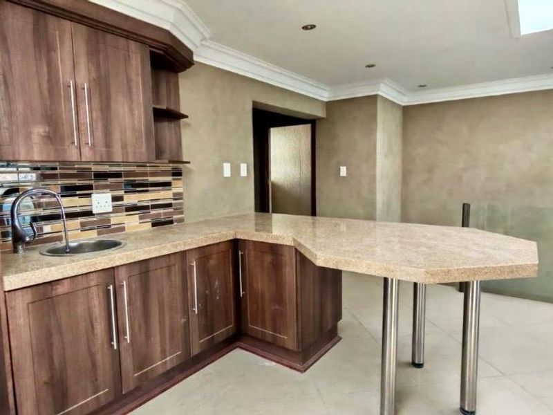 A clean, empty kitchen featuring wood-look cabinetry, a mosaic tile backsplash, and a functional breakfast bar with stainless steel support legs.