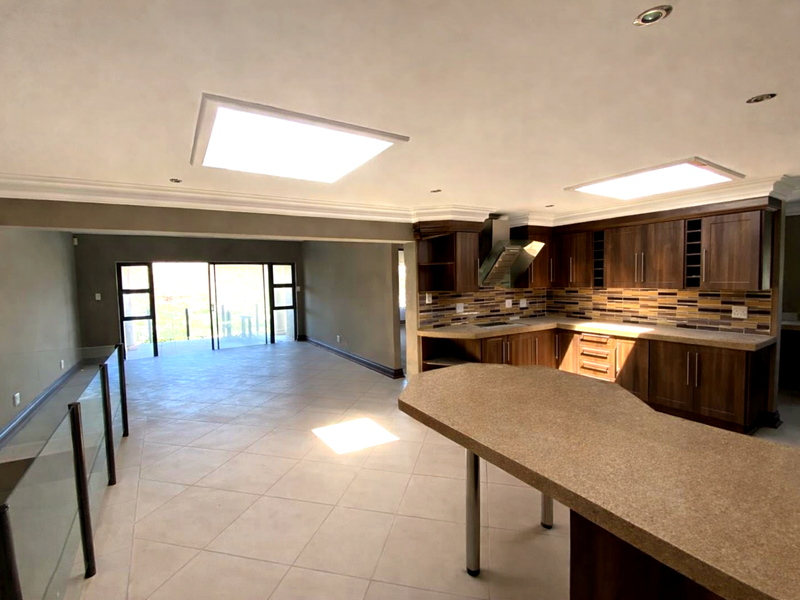 Spacious open-plan kitchen and living area featuring dark wood cabinetry, stone countertops, recessed lighting, skylights, and large sliding doors leading to an outdoor space.