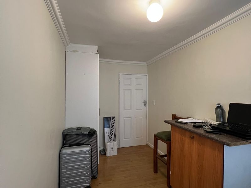 A functional room featuring laminate flooring, crown molding, and a built-in storage cupboard, suitable for use as a home office or study area.