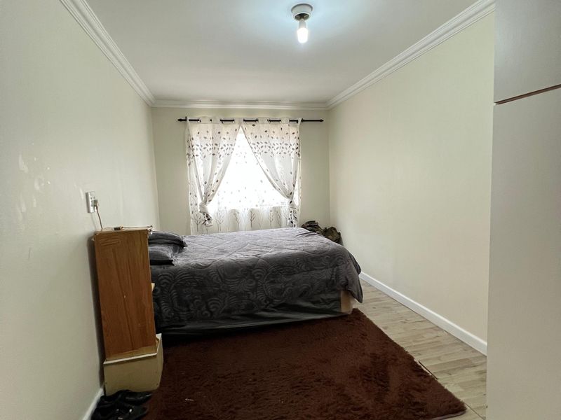 A standard bedroom featuring laminate flooring, crown molding, and a built-in cupboard, offering a functional space with neutral wall finishes.