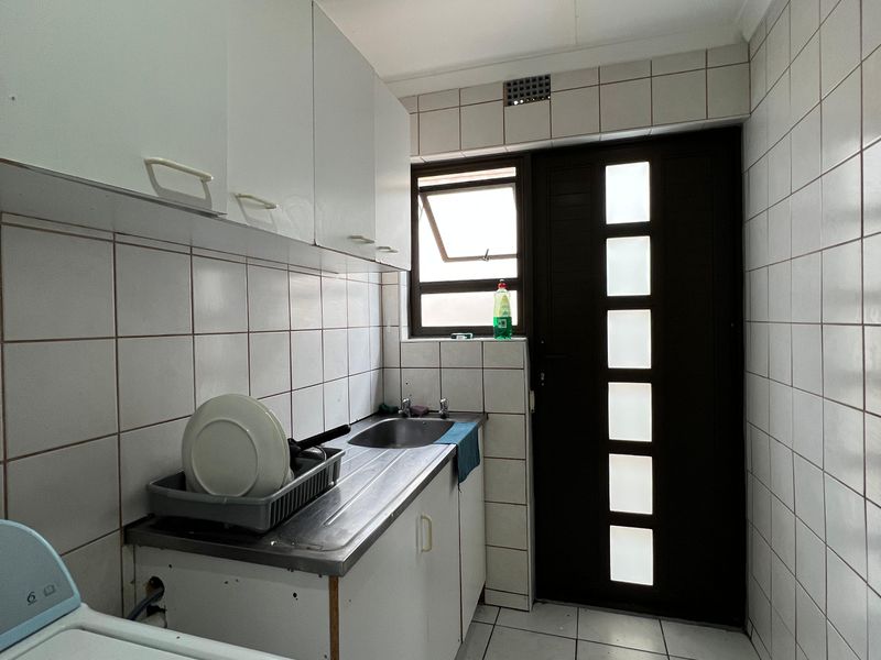 A functional laundry room featuring tiled walls and flooring, built-in cabinetry, a stainless steel sink, and direct access to the exterior.