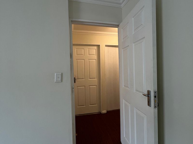A clean, neutral hallway featuring laminate flooring, crown molding, and classic panelled interior doors leading to adjacent rooms.