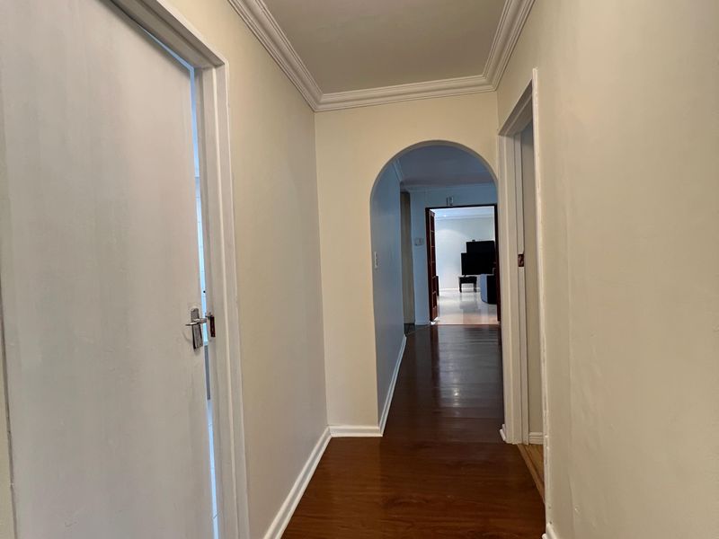 A clean, well-maintained hallway featuring laminate flooring, decorative ceiling cornices, and an arched transition leading to adjacent living spaces.