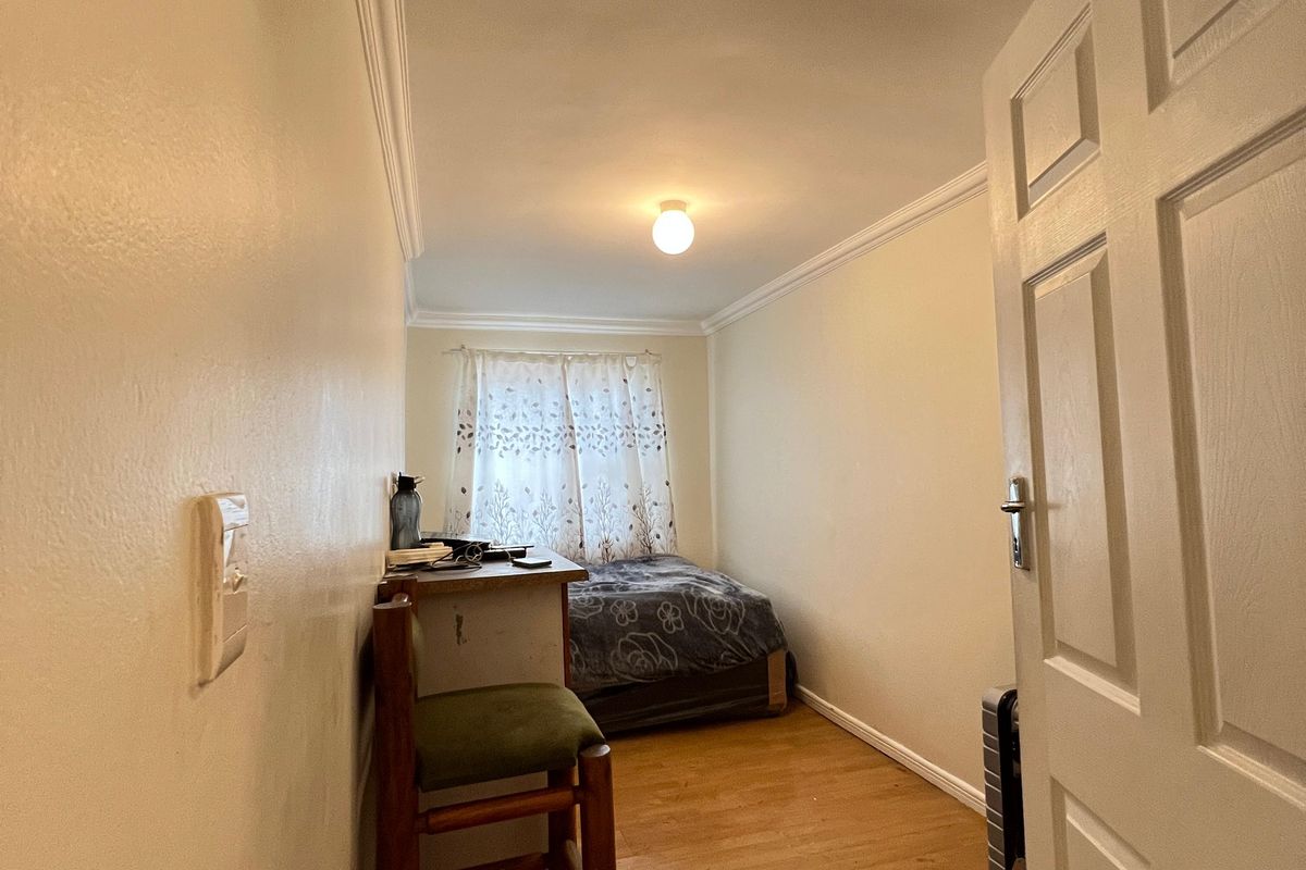 A compact bedroom featuring laminate flooring, crown molding, and a neutral color palette, offering a functional space with natural light.