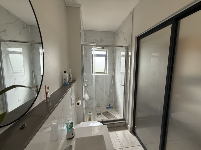 Modern bathroom featuring a walk-in shower with glass enclosure, marble-look wall tiling, and a sleek vanity basin.
