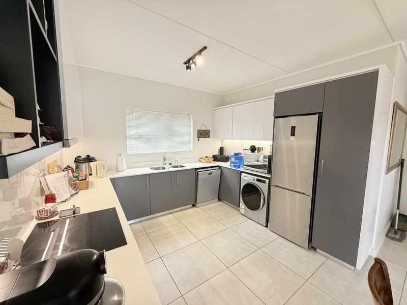 Modern kitchen featuring sleek grey and white cabinetry, integrated appliances, tiled flooring, and ample counter space with a functional layout.