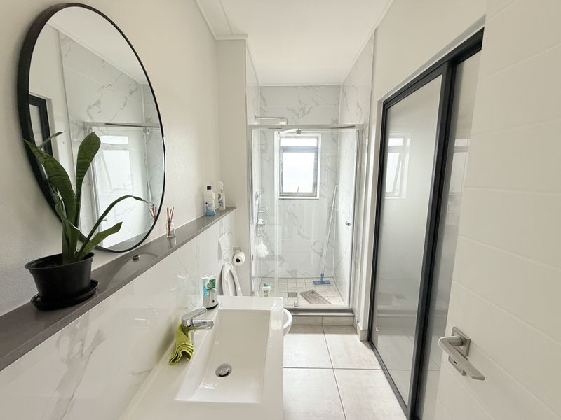 Modern bathroom featuring a glass-enclosed shower, sleek vanity basin with mixer tap, and contemporary marble-look wall tiling.