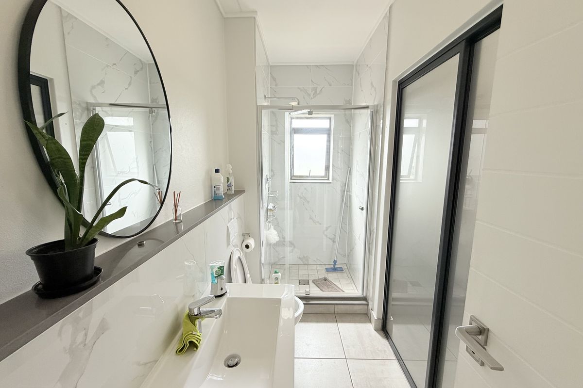 Modern bathroom featuring a glass-enclosed shower, sleek vanity basin with mixer tap, and contemporary marble-look wall tiling.