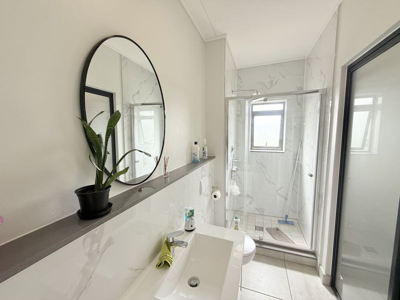 Modern bathroom featuring a vanity basin with mixer tap, built-in shelf, and a glass-enclosed shower with marble-look wall tiling.