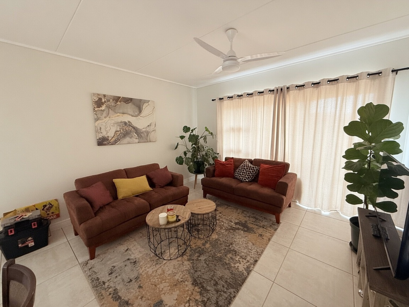A well-maintained living room featuring neutral tiled flooring, a ceiling fan, and large window treatments allowing for natural light.