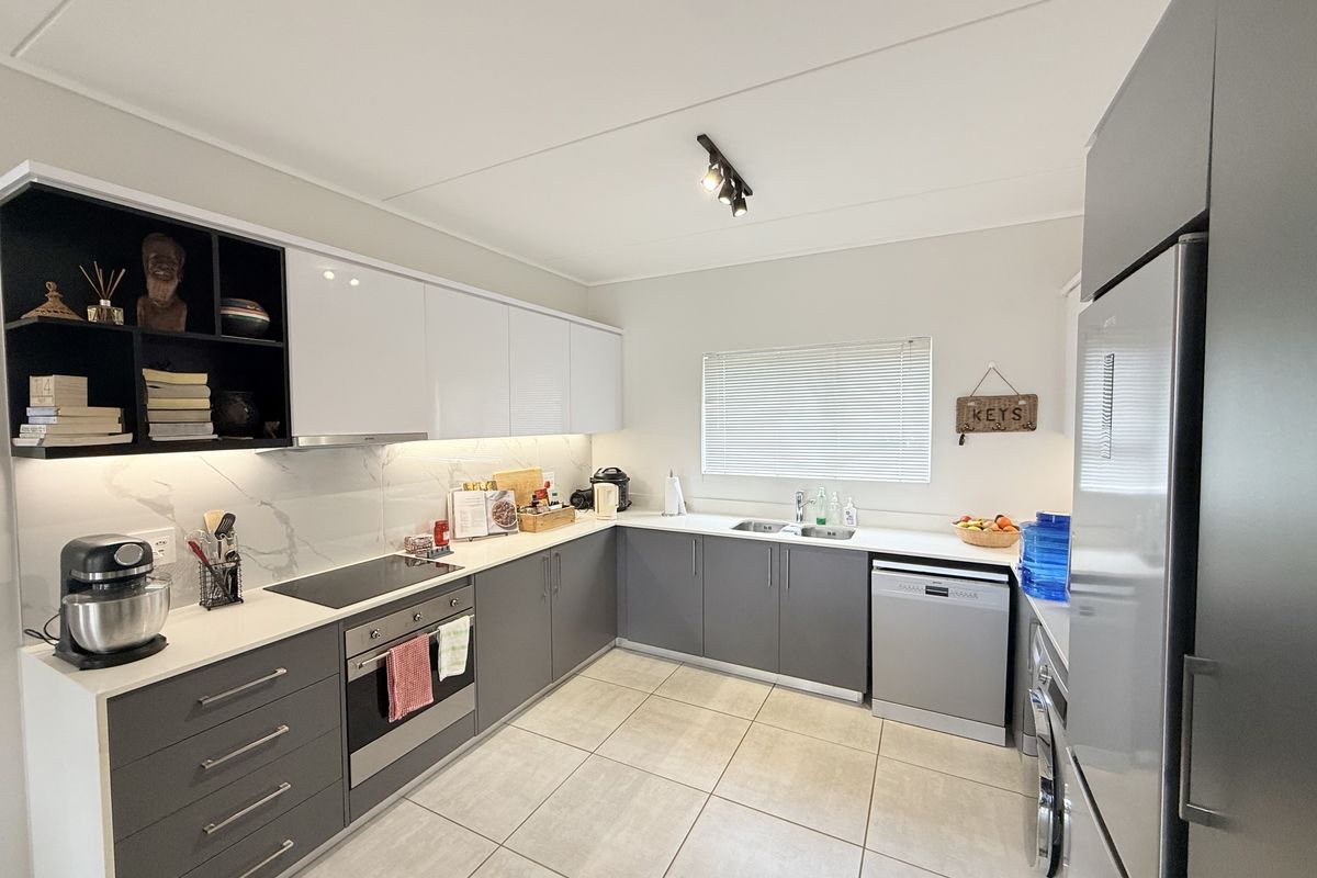 Modern kitchen featuring sleek grey and white cabinetry, stone countertops, integrated appliances, and tiled flooring with ample workspace and under-cabinet lighting.