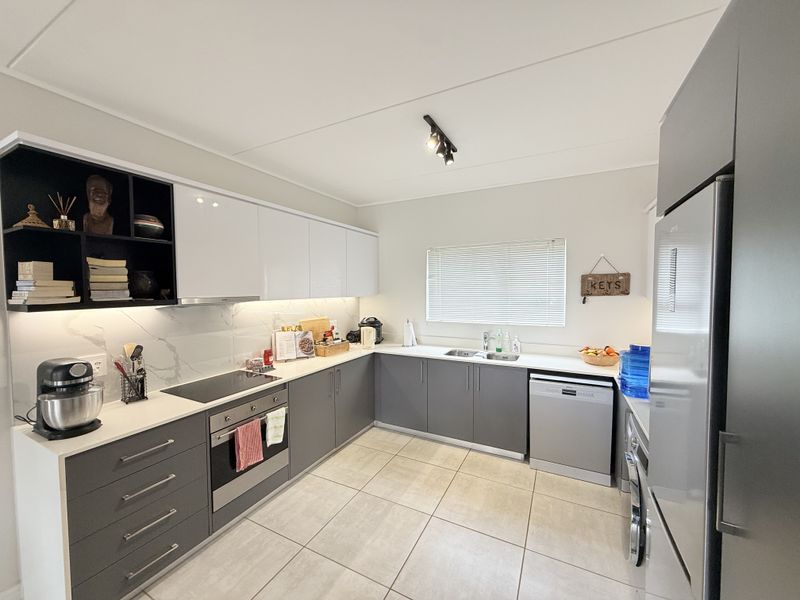 Modern kitchen featuring sleek grey and white cabinetry, stone countertops, integrated appliances, and tiled flooring with ample workspace and under-cabinet lighting.