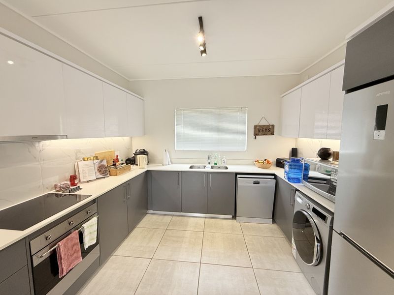 Modern kitchen featuring sleek white and grey cabinetry, stone countertops, integrated appliances, and high-quality tiled flooring with efficient under-cabinet lighting.