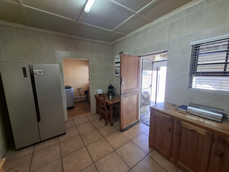 A functional kitchen featuring tiled walls and flooring, wooden cabinetry, and a stable door leading to the exterior, with an adjacent laundry area.