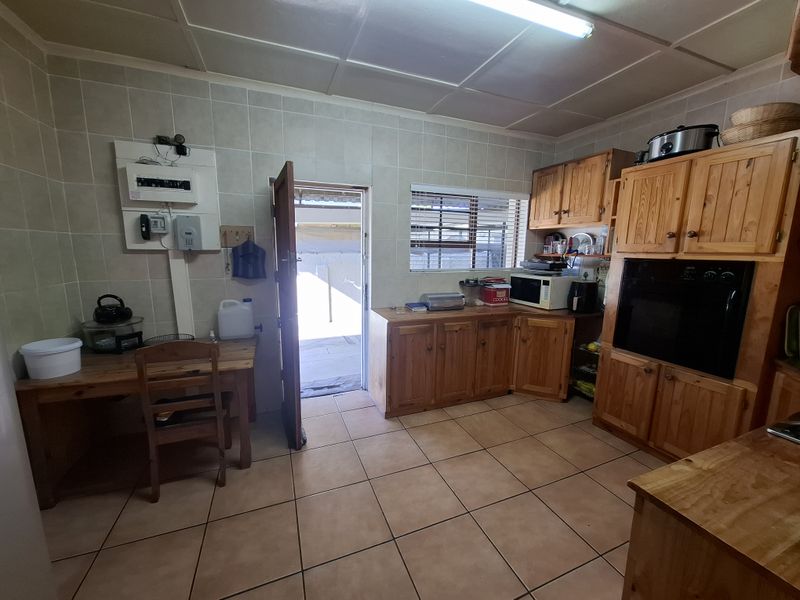 A functional kitchen featuring wooden cabinetry, tiled walls and flooring, and a built-in oven, with direct access to an outdoor area.
