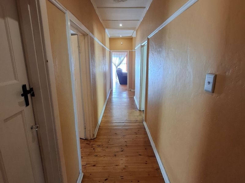 A long, empty hallway featuring original timber flooring, traditional skirting boards, and a ceiling rose, providing access to multiple rooms.