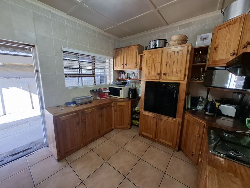A functional kitchen featuring traditional wooden cabinetry, built-in oven, gas hob, and tiled finishes with direct access to an outdoor area.