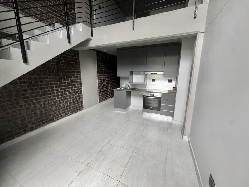 Modern kitchen area featuring built-in cabinetry, integrated oven, and extractor fan, set against an exposed brick wall with an adjacent staircase.