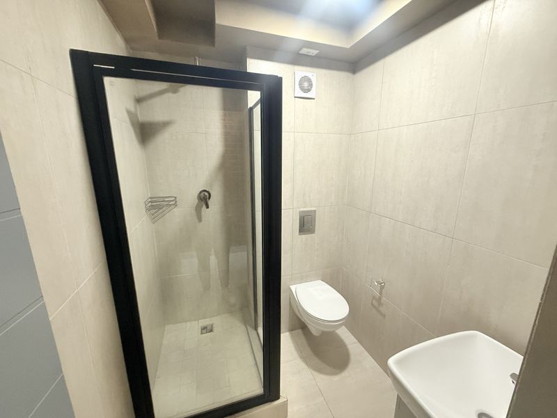 Modern bathroom featuring a walk-in shower with black frame, wall-mounted toilet with concealed cistern, and neutral floor-to-ceiling tiling.