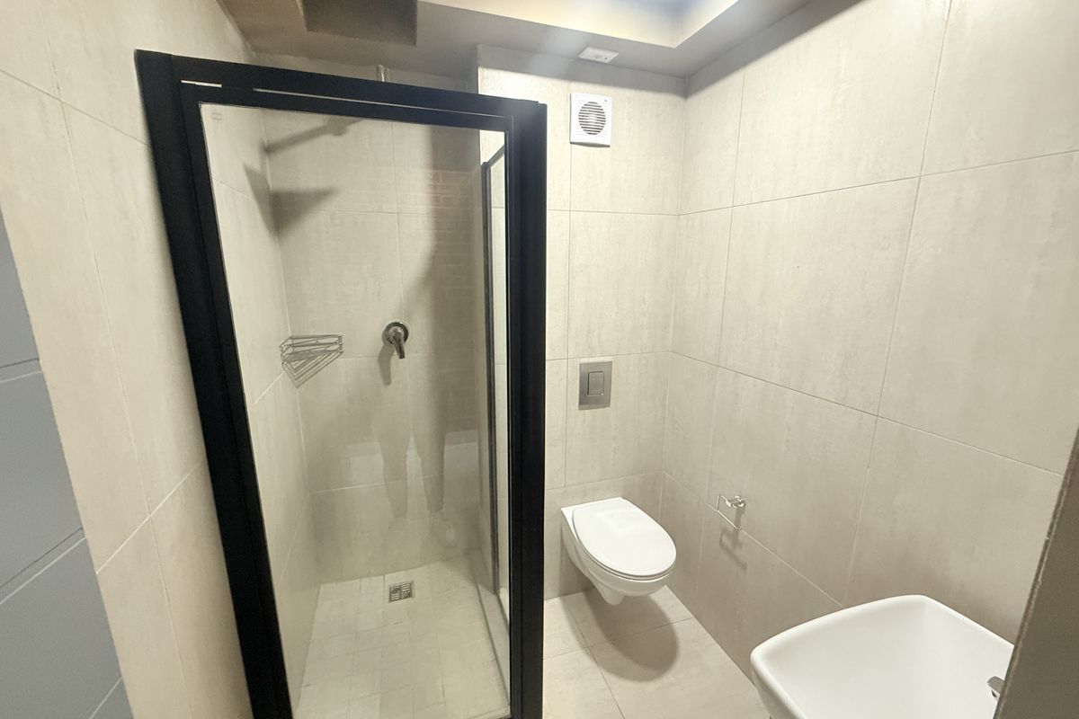 Modern bathroom featuring a walk-in shower with black frame, wall-mounted toilet with concealed cistern, and neutral floor-to-ceiling tiling.