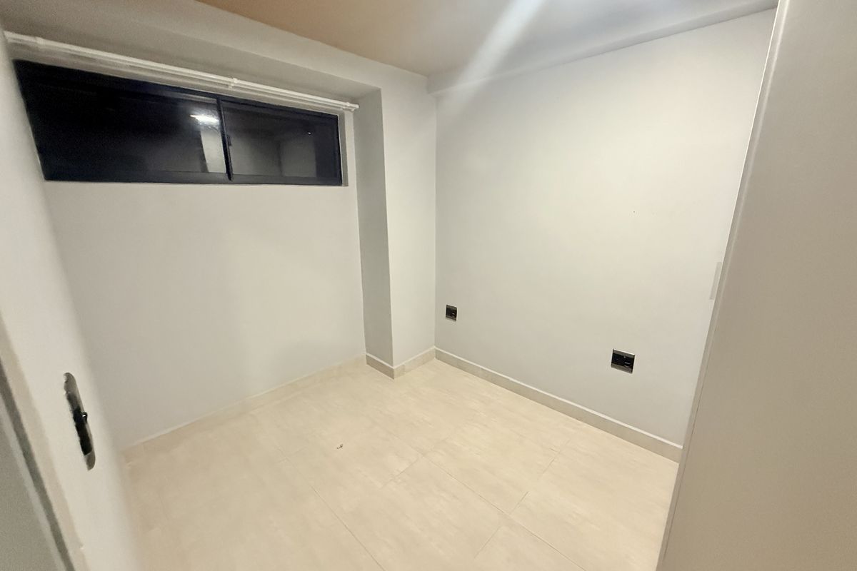 A clean, empty bedroom featuring neutral tiled flooring, a sliding window, and modern electrical outlets, ready for personalization.