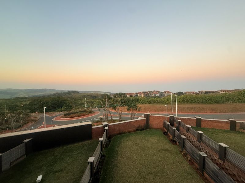 Elevated view overlooking a landscaped garden area, brick boundary walls, and the surrounding estate neighborhood at sunset.