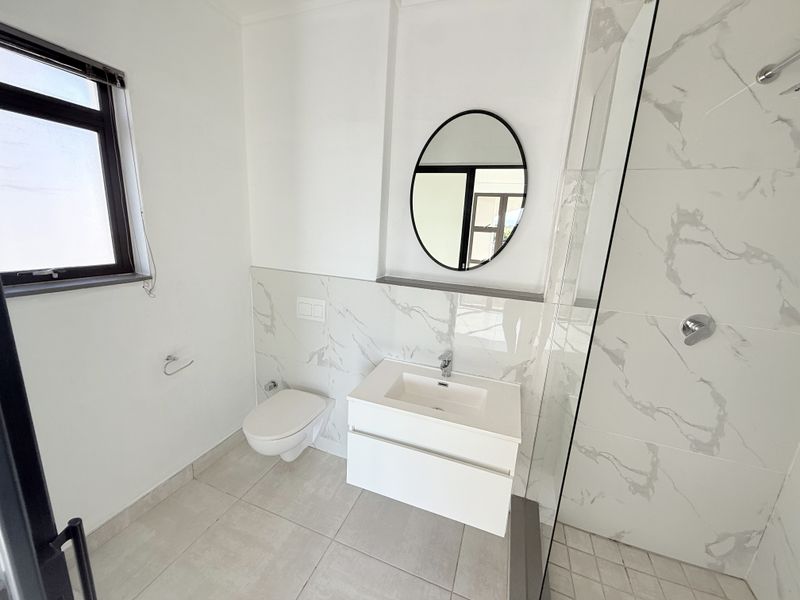Modern bathroom featuring a wall-mounted toilet, sleek vanity with integrated basin, and a spacious shower with marble-look tiling.